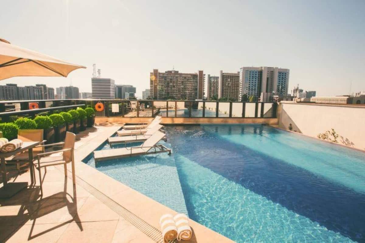 Una piscina en la azotea con sillas de descanso y un horizonte urbano al fondo.