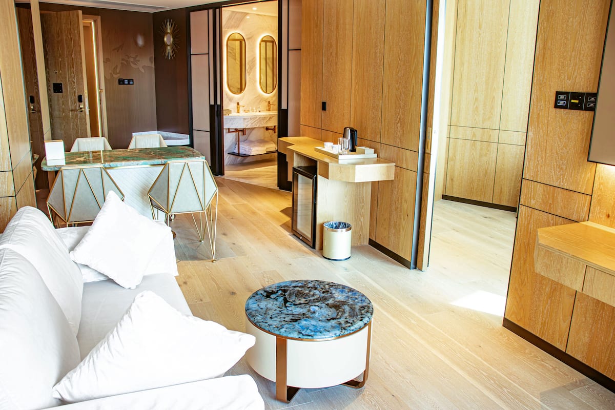 Une chambre d’hôtel moderne avec un canapé blanc, une table basse ronde et un comptoir d’accueil en bois.