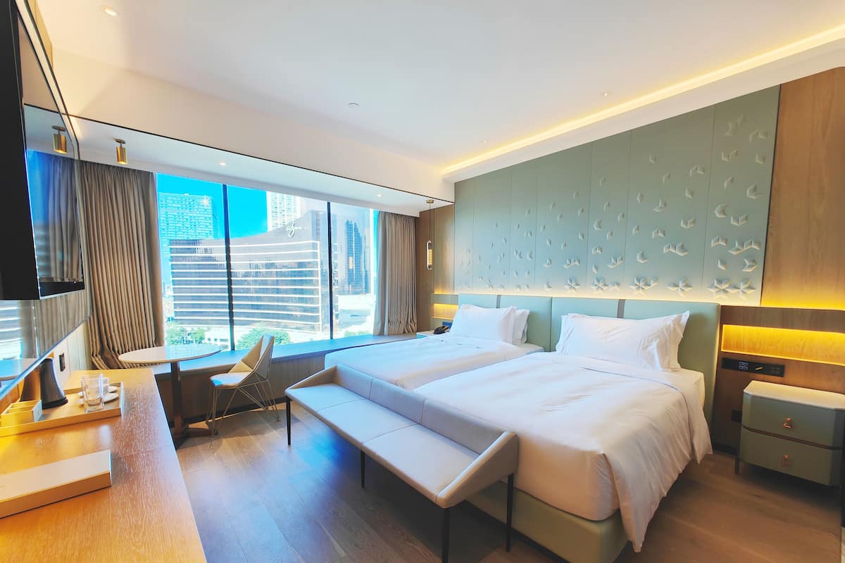 Une chambre d’hôtel moderne avec deux lits, un bureau, une chaise et une vue sur le paysage urbain.