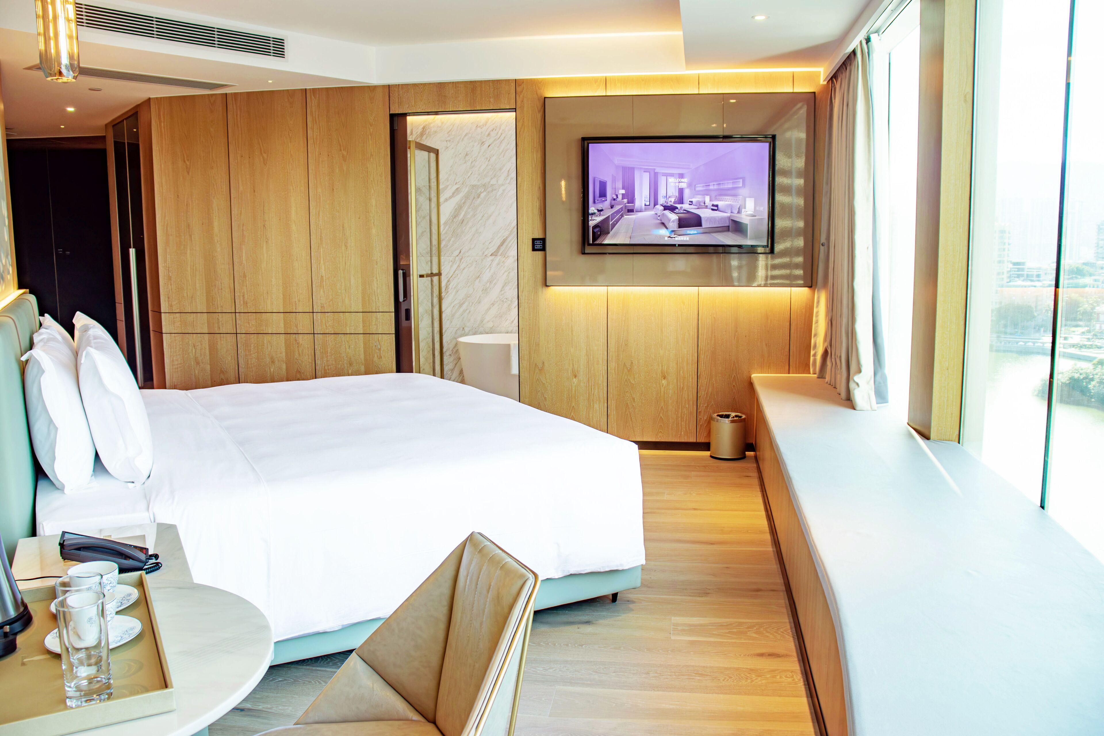 Habitación de hotel moderna con una cama grande, un televisor montado en la pared, un revestimiento de pared de madera y una ventana con vistas a la ciudad.