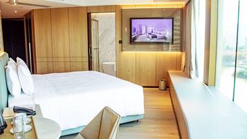 Habitación de hotel moderna con una cama grande, un televisor montado en la pared, un revestimiento de pared de madera y una ventana con vistas a la ciudad.
