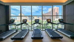 Un gimnasio con cinco cintas de correr alineadas, ventanas amplias que ofrecen vista a la ciudad.