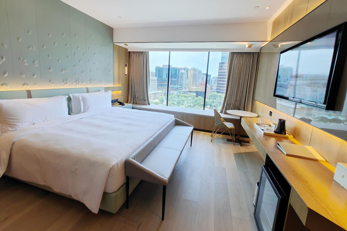 Une chambre d’hôtel moderne, dotée d’un grand lit, d’un bureau et offrant une vue sur le paysage urbain.