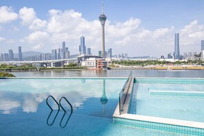 Une piscine à l’eau d’un bleu cristallin, une haute tour en arrière-plan et le profil d’une ville.