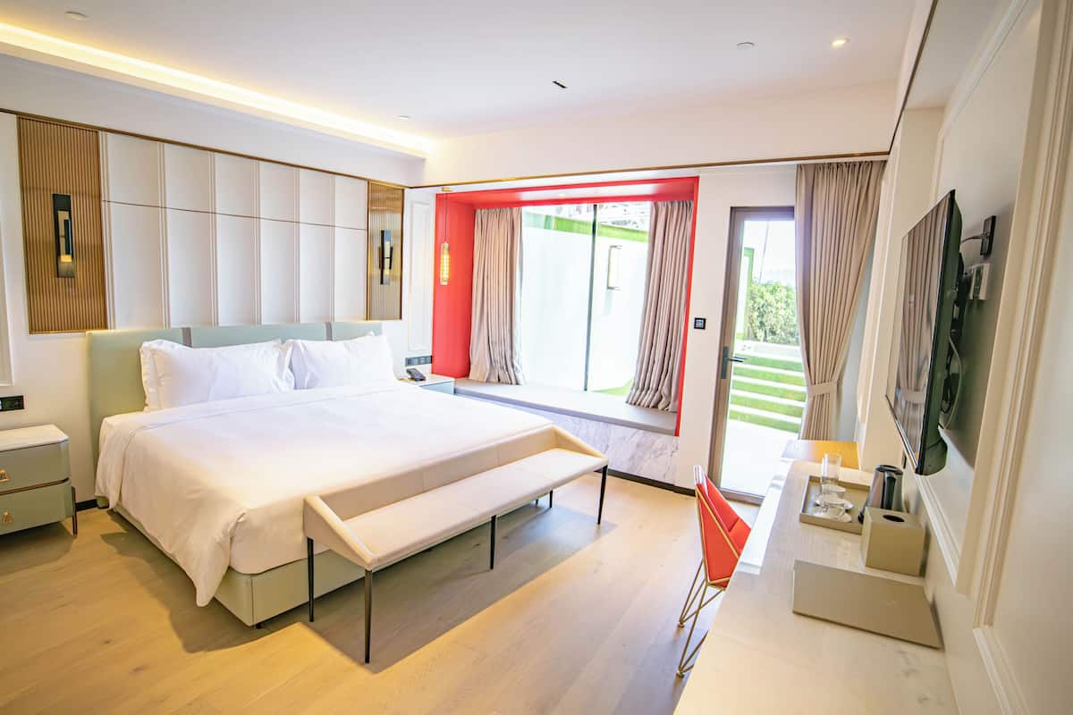 Une chambre d’hôtel moderne, dotée d’un grand lit, d’une banquette, d’un bureau et d’une télévision.
