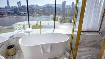 Un baño moderno con una bañera independiente, suelo de mármol y vistas a la ciudad a través de amplias ventanas.