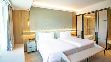 A modern hotel room with a large bed, bedside tables, a bench, and a walk-in closet.