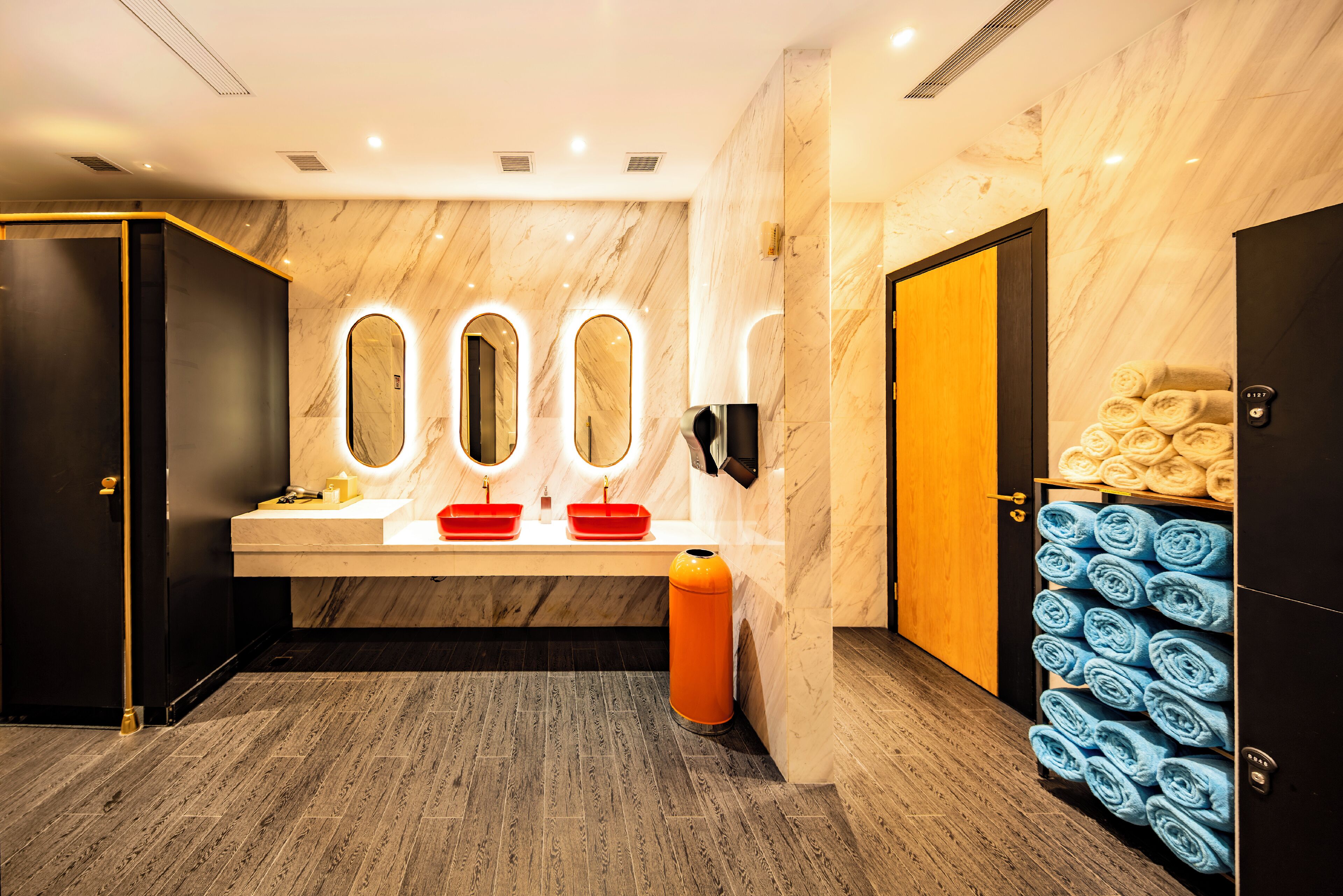 Ett modernt badrum med väggar i marmor, en tvättställsmöbel med tre tvättställ och en handduksställare med prydligt hoprullade handdukar.