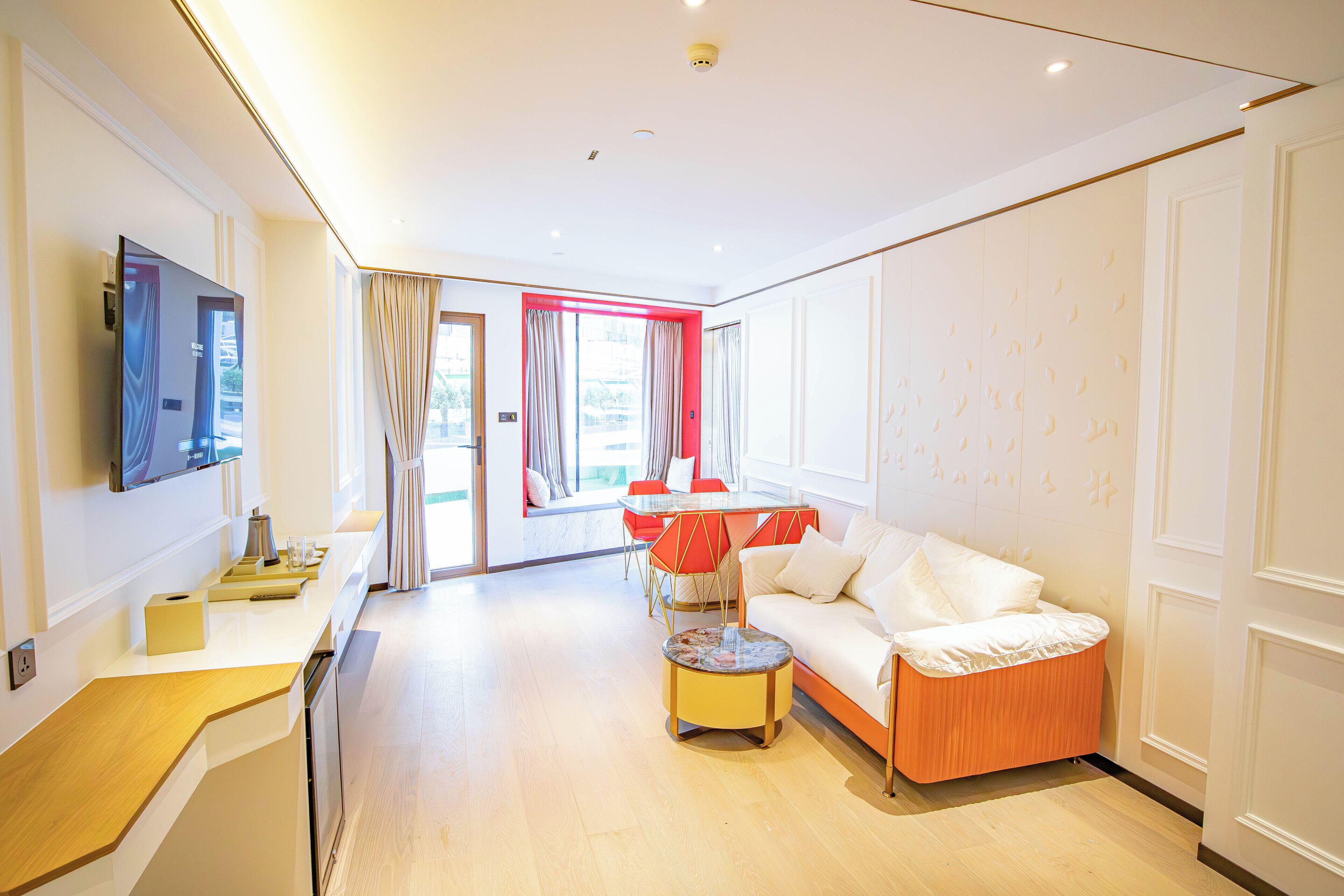 Een moderne hotelkamer met een houten vloer, een bank, een kleine ronde tafel en een aan de muur bevestigde televisie.
