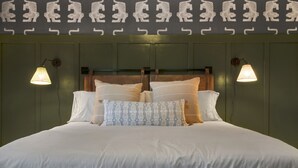 A neatly made bed with white linens and patterned pillows, flanked by wall-mounted lamps.