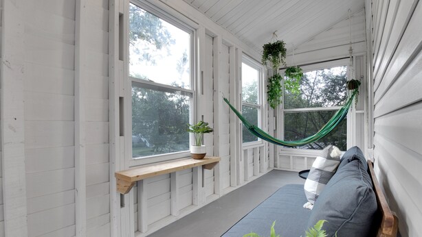A porch with a bench, a hammock, and potted plants.