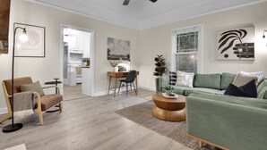A modern living room with a green sofa, a wooden coffee table, and a dining area with a wooden table and chairs.