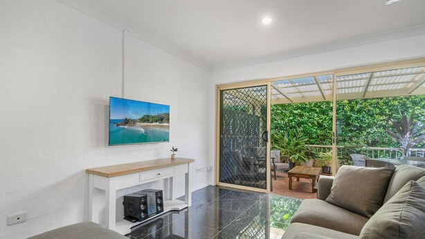 Een moderne woonkamer met een flatscreen televisie aan de muur, een open haard en een grote schuifpui die uitkomt op een balkon met planten.