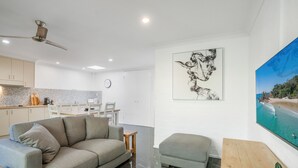 Een moderne woonkamer met een grijze bank, een klein poufje, een houten salontafel en een schilderij van een strand.