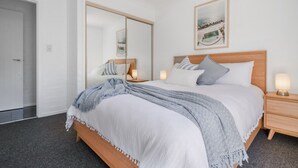 Een slaapkamer met een bed, nachtkastjes, een spiegel en een lijst met een afbeelding aan de muur.