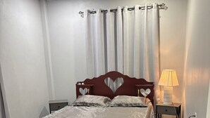 A bedroom with a bed, a nightstand, a lamp, and a window with curtains. - In City - Minutes to Regent St, Botanical Gardens, Cuffy Sq, and Bourda Market.  (Georgetown)