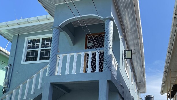 A two-story building with a balcony, a window with a metal grill, and a water tank on the roof. - In City - Minutes to Regent St, Botanical Gardens, Cuffy Sq, and Bourda Market.  (Georgetown)
