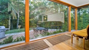 Un intérieur moderne avec de grandes fenêtres donnant sur un jardin avec un barbecue et du mobilier de jardin.