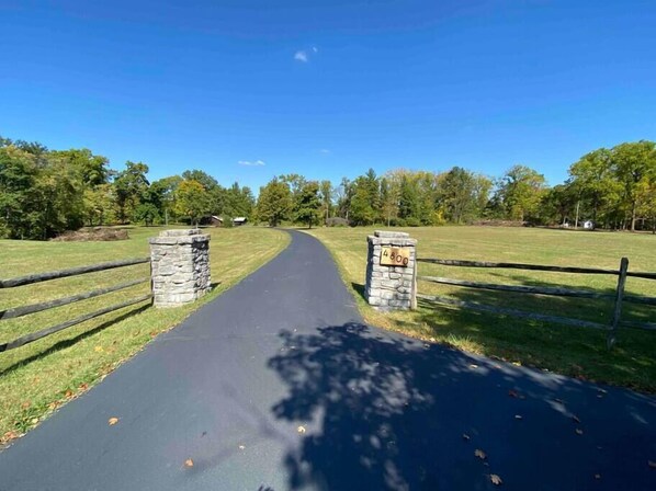 A paved pathway leading to a stone gate with a number sign, surrounded by a grassy area and trees.