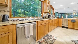 Une cuisine moderne avec des meubles en bois, des appareils électroménagers en acier inoxydable et une grande fenêtre donnant sur la forêt.
