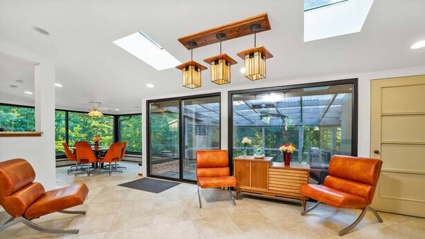 Un intérieur moderne avec des fauteuils en cuir, un meuble en bois et de grandes fenêtres donnant sur un paysage verdoyant.