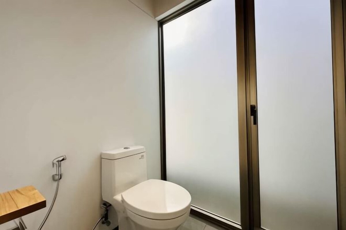 A bathroom with a toilet, a wooden shelf, and a frosted glass door.