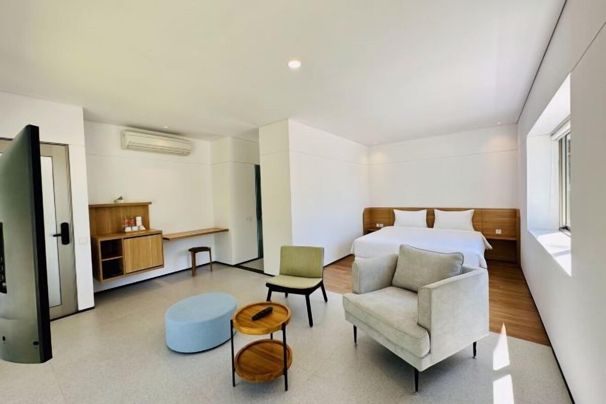 A modern hotel room with a bed, a seating area with a sofa and chairs, a small table, and a built-in desk.