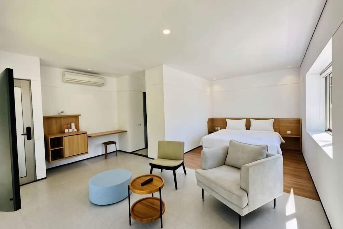 A modern hotel room with a bed, a sofa, a chair, a small table, and a wardrobe.
