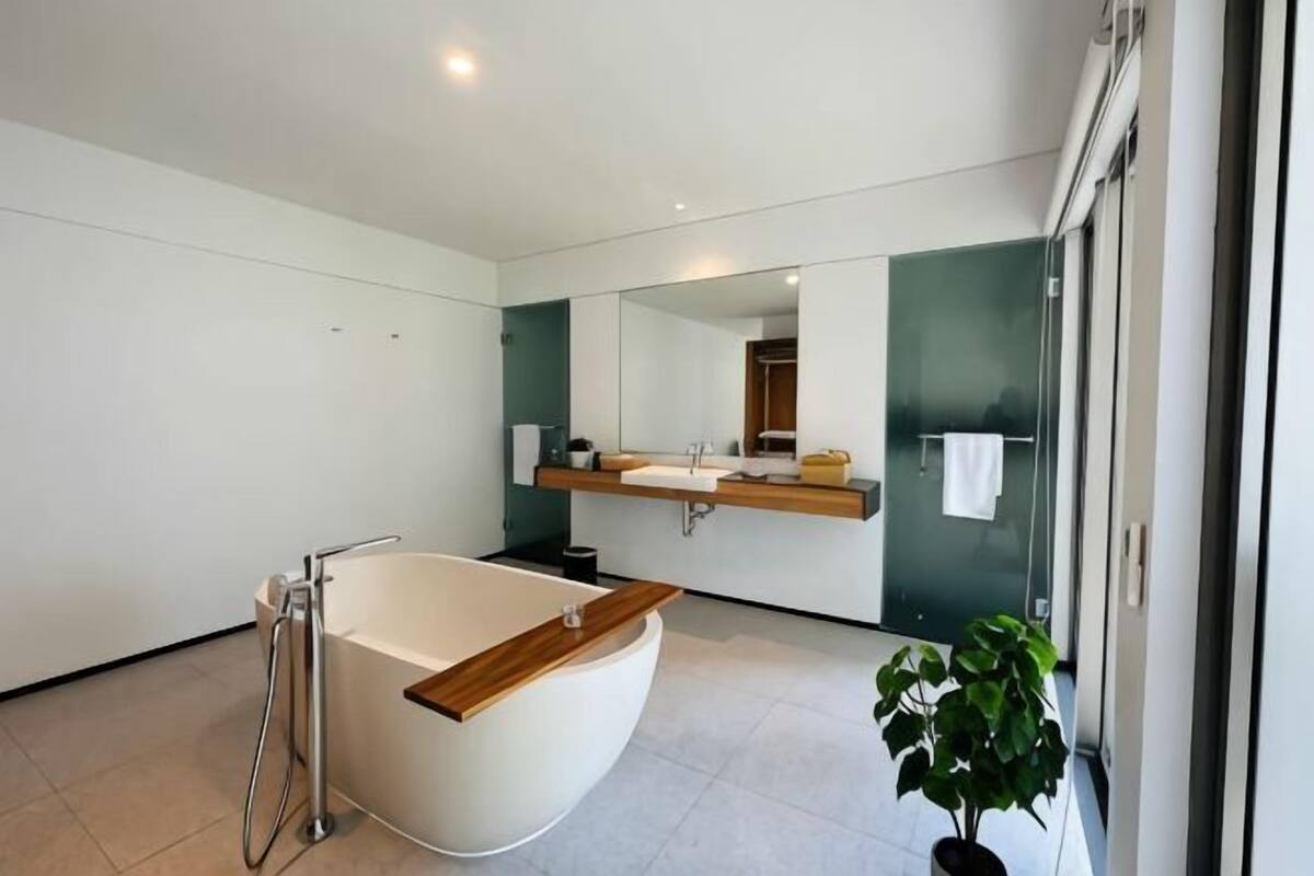 A modern bathroom with a freestanding bathtub, a large mirror, and a potted plant.