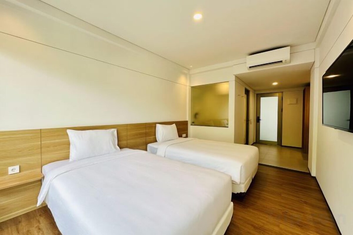 A hotel room with two beds, a wooden headboard, a mirror, and a door leading to another room.