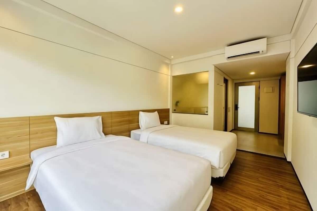 A hotel room with two beds, a wooden headboard, a large mirror, and an air conditioning unit.