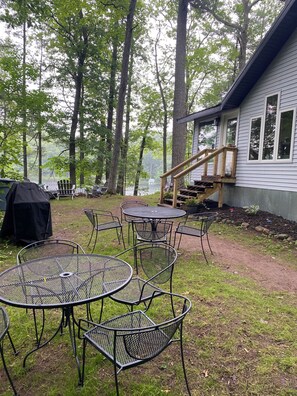 Ein Garten mit überdachter Grillstation, Metalltischen und -stühlen sowie einer Holzterrasse, die zu einem Haus führt.