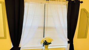 Une pièce avec deux fauteuils marron, une petite table en bois ornée d’un vase de fleurs jaunes, et une fenêtre avec des stores blancs et des rideaux noirs.