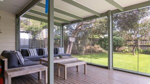Un espace extérieur aménagé, abrité et doté d’une terrasse en bois, d’un ensemble de canapés et d’une table basse.