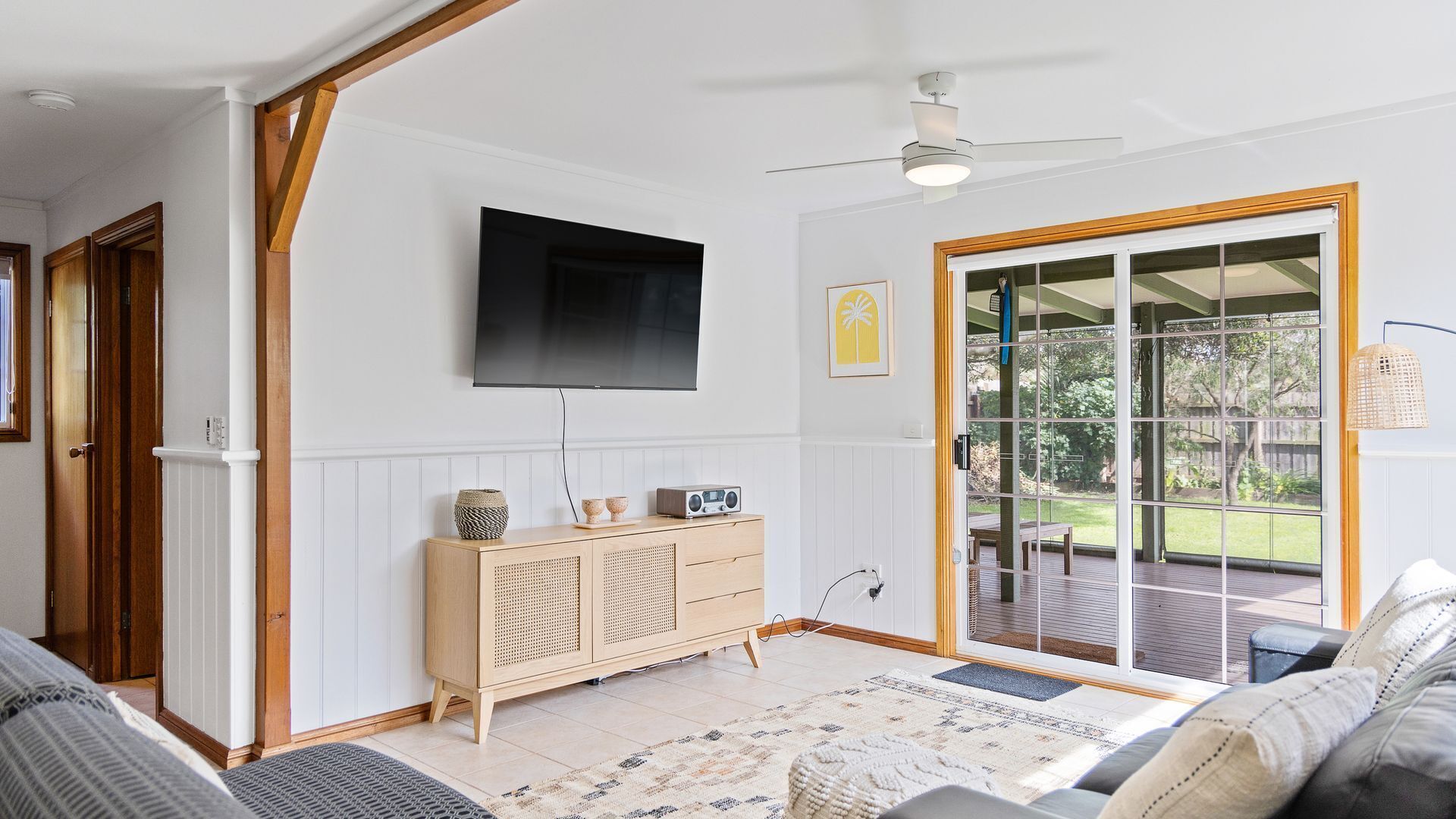 A living room with a flat-screen TV, wooden furniture, and a sliding glass door leading to an outdoor area.
