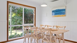 Un coin repas avec une table et des chaises en bois, de grandes fenêtres donnant sur un paysage verdoyant et un tableau accroché au mur.