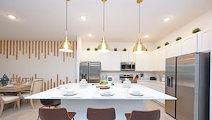 Una cocina moderna con armarios blancos, electrodomésticos de acero inoxidable y una isla central con taburetes de bar.