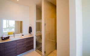 A modern bathroom with a large mirror, two sinks, a glass shower enclosure, and a wooden vanity.