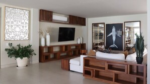 Una sala de estar moderna con una televisión de pantalla plana, estanterías de madera, un sofá blanco y obras de arte decorativas.