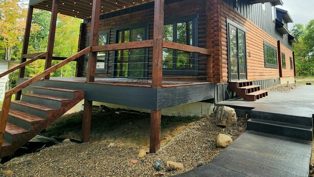 A modern log cabin with a covered porch, large windows, and a stone foundation.