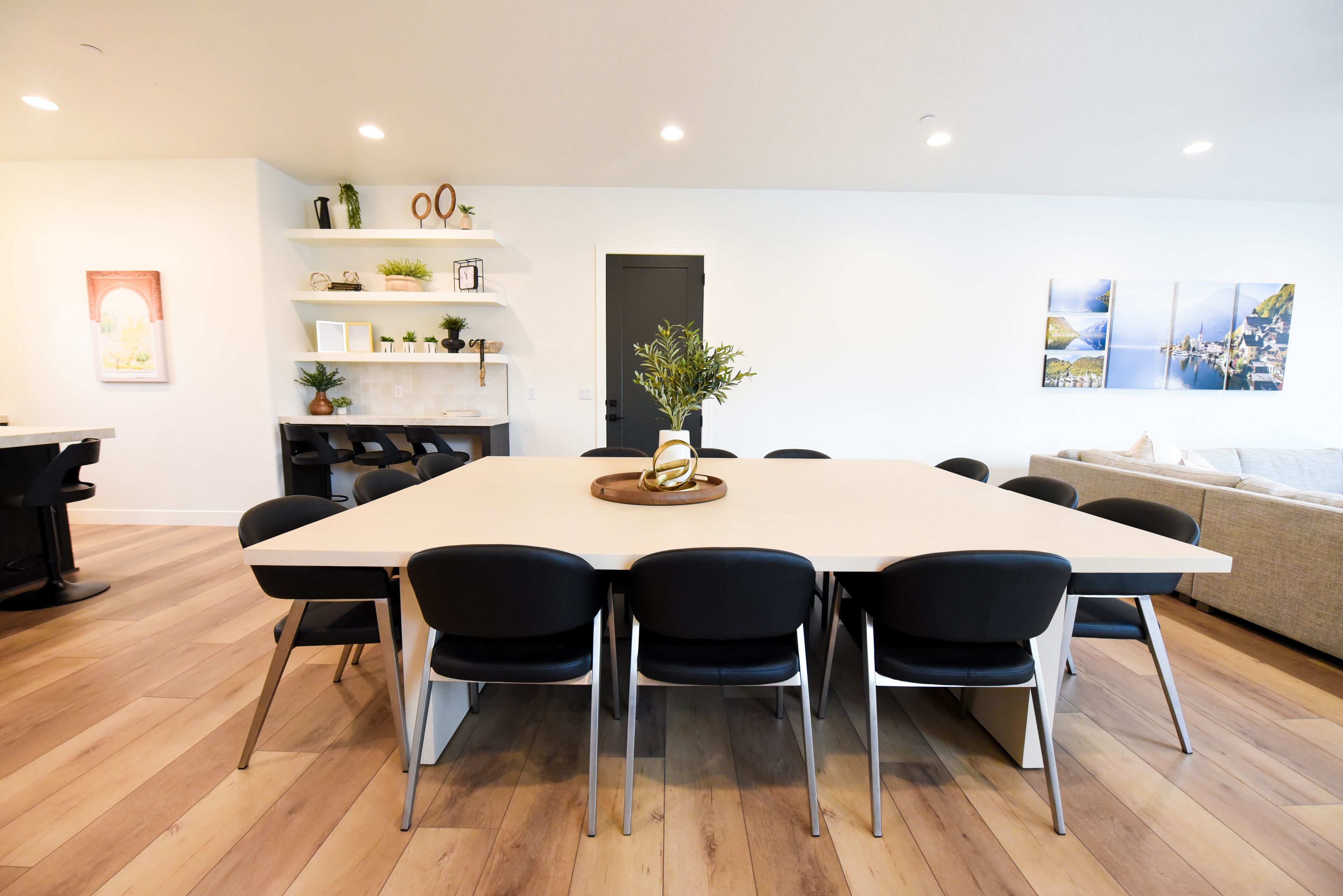 A modern dining area with a large table, black chairs, and a wooden floor.