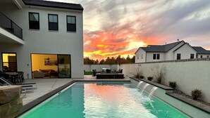 Une maison moderne dotée d’une piscine, d’un patio avec mobilier d’extérieur et offrant une vue sur le coucher de soleil.