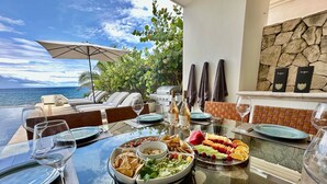 Una mesa de comedor dispuesta con platos, vasos y una variedad de alimentos, incluyendo una bandeja de frutas, tazones de guacamole y totopos.