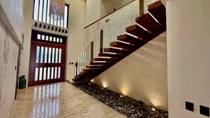 Un interior moderno con suelo de mármol, una escalera de madera y una puerta grande de madera con listones verticales.