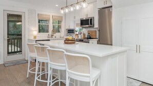 A modern kitchen with white cabinetry, a large island with bar stools, a stainless steel refrigerator, and a microwave. - Sundays at the Millers - BOTH CLUBS (Bald Head Island)
