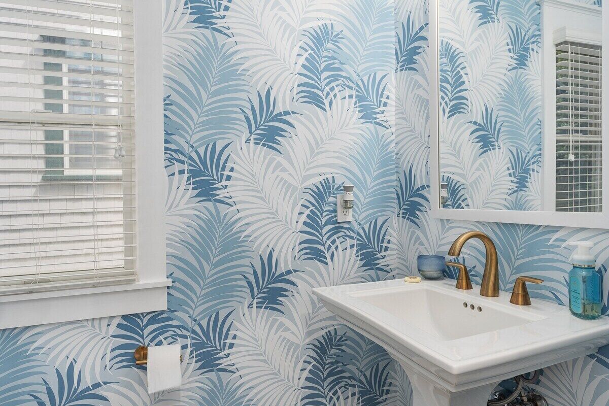 Een badkamer met een witte wastafel, een spiegel en een raam met zonwering.