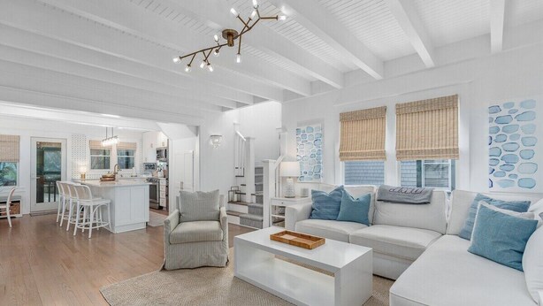 A modern living room with a white sofa, a coffee table, and a dining area with a kitchen in the background. - Sundays at the Millers - BOTH CLUBS (Bald Head Island)