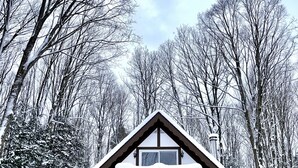 A two-story cabin with a balcony, surrounded by snow-covered trees. - Relax at the Cozy Cabin, just a 5-min drive to it all (Harbor Springs)