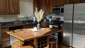 A kitchen with wooden cabinets, a stainless steel refrigerator, a microwave, and a wooden island with stools.
