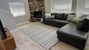 A living room with a stone fireplace, a sectional sofa, and a television on a wooden stand.
